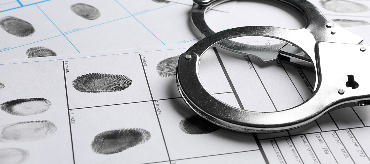 This is a stock photo from Shutterstock. This is an up close image of finger prints and handcuffs on a formal arrest record. 